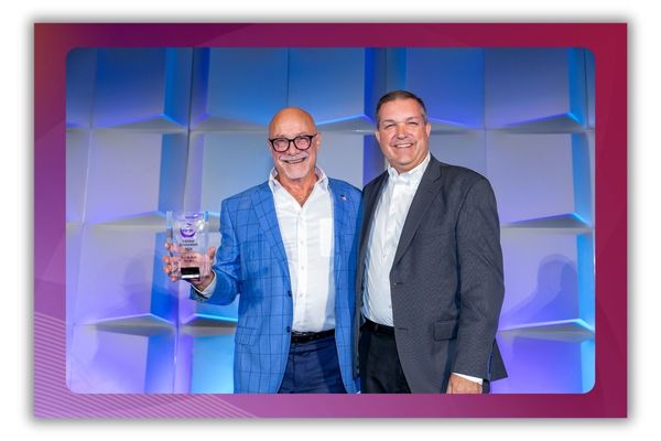 A photo of two men smiling and standing on a stage. One of the men is holding an award.