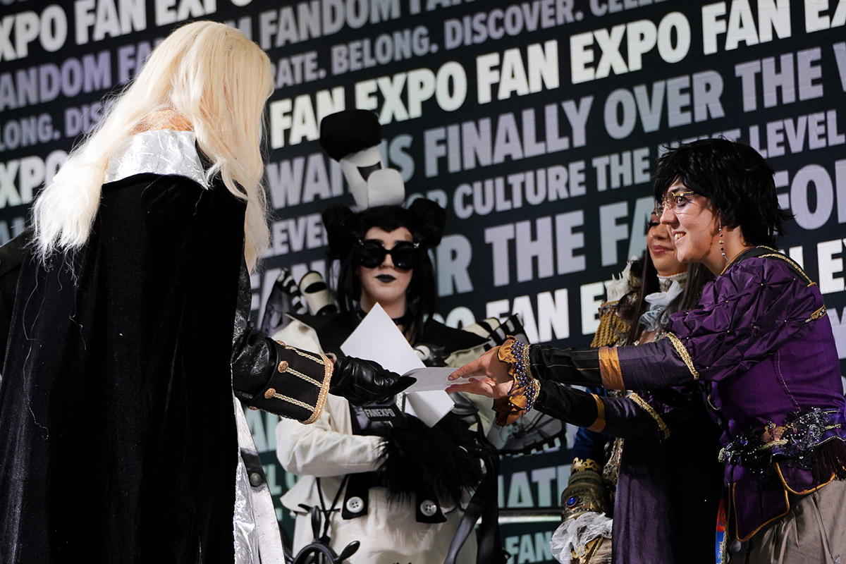 a cosplayer hands another cosplayer a paper award