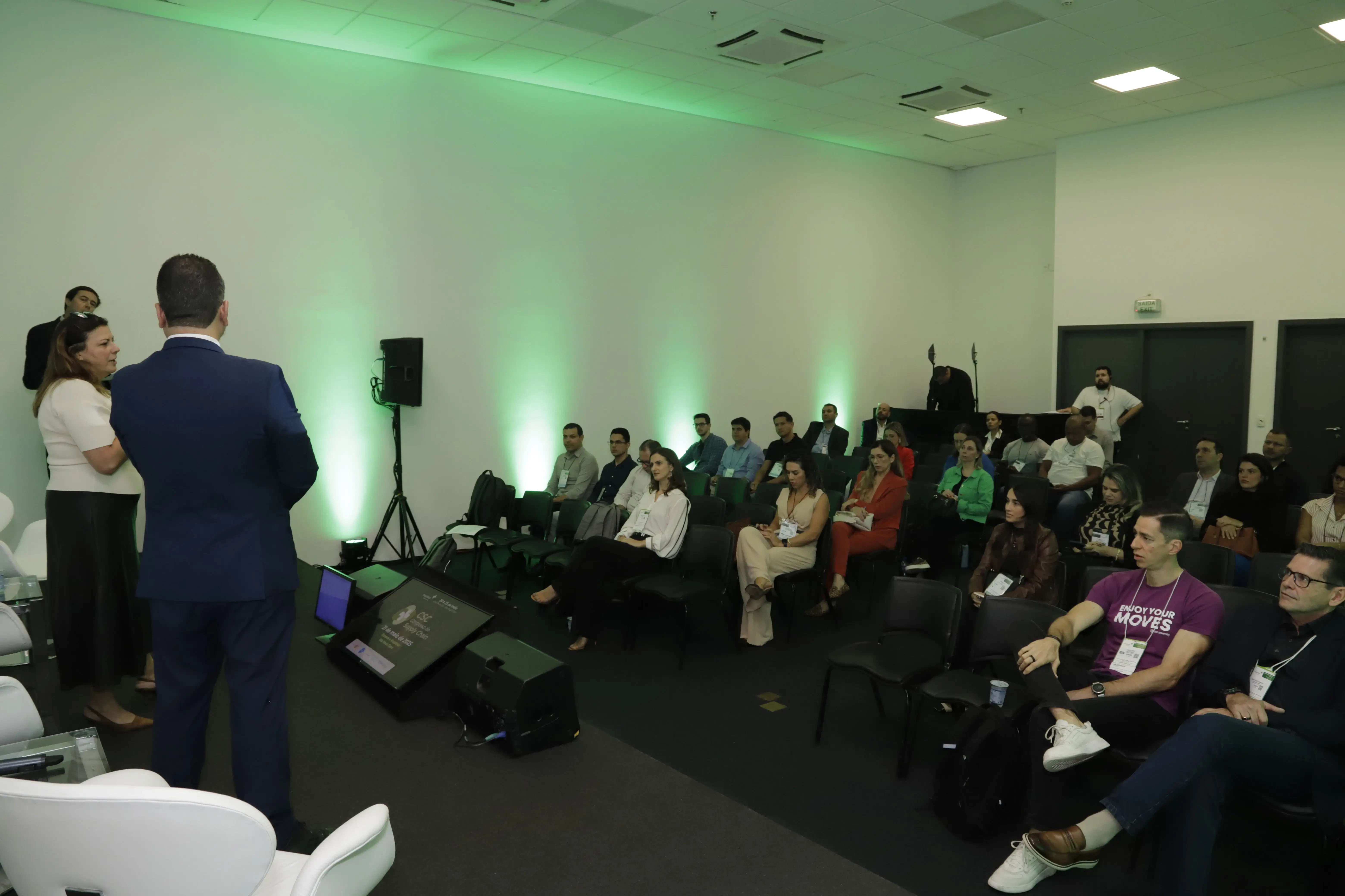 Visão geral da sala de conferência no CSC - Congresso de Supply Chain durante a Hospitalar. Palestrantes em diálogo com o público em um ambiente corporativo moderno, com foco na plateia sentada e organização do auditório.