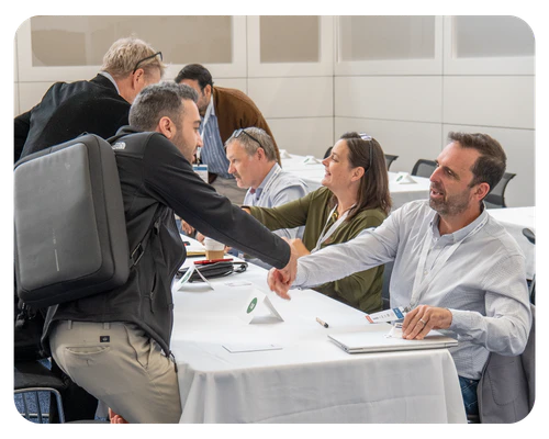 At a conference table, a man shakes hands with another, highlighting networking opportunities at the 'Curated Ways to Connect' event.
