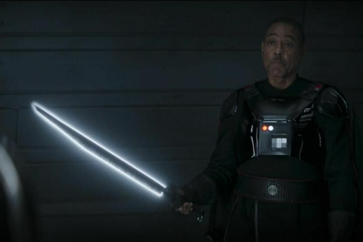 A man in a tech filled dark armour suit holds a glowing black & white blade extended from his arm