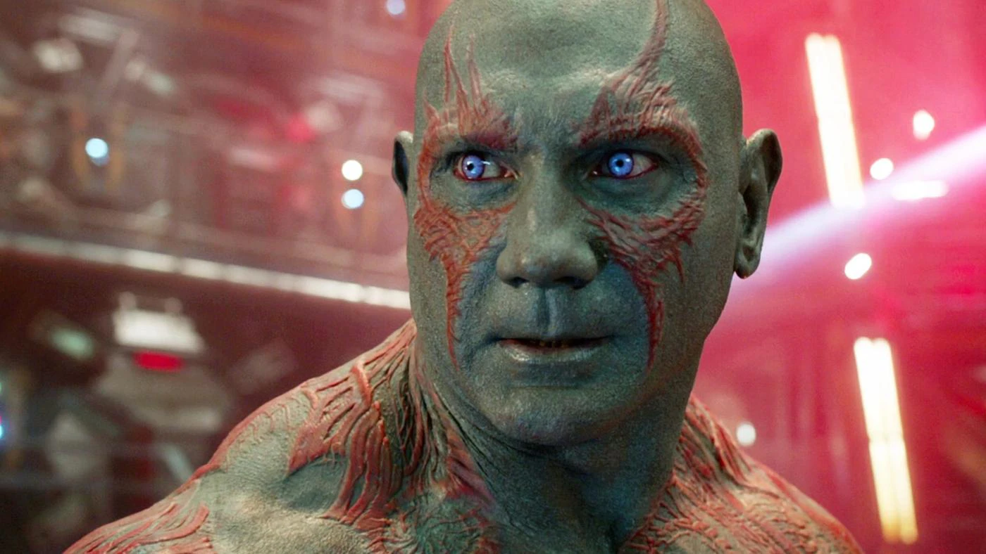 Drax has piercing blue eyes and is looking off into the distance. He looks concerned.