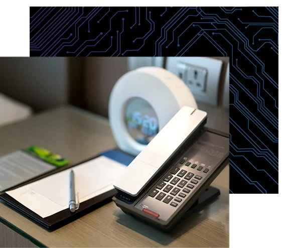 Phone, alarm clock, electrical outlets, and notepad with pen on a hotel's room night stand
