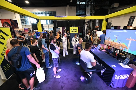 Fans gather to watch other fans 1V1 members of the US Navy at their booth. The game in play on the large television is Super Mario.