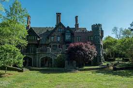 A distant shot of the large brick home. Its plentiful windows full of sunlight, and the grass and trees a bright vibrant green.