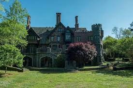 A distant shot of the large brick home. Its plentiful windows full of sunlight, and the grass and trees a bright vibrant green.
