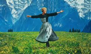 Maria spins, arms extended amongst the German mountain side, in a plush green field full of flowers.