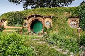 A distant shot of Bag End. The lush grass and greenery encapsulates the whole home - the round green door is ajar.