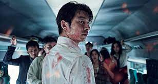 A man stands bloodied with his back to the camera. On lookers behind him on the train are also bloodied and are horrified.