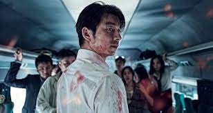 A man stands bloodied with his back to the camera. On lookers behind him on the train are also bloodied and are horrified.