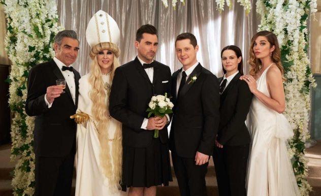 The entire cast of Schitt's Creek stands in formal tuxedos and dresses at the wedding altar