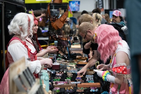 Fans shop the Misty Mountain Gaming Booth and browse new dice. The people manning the booth are dressed as a red and a white tiefling.
