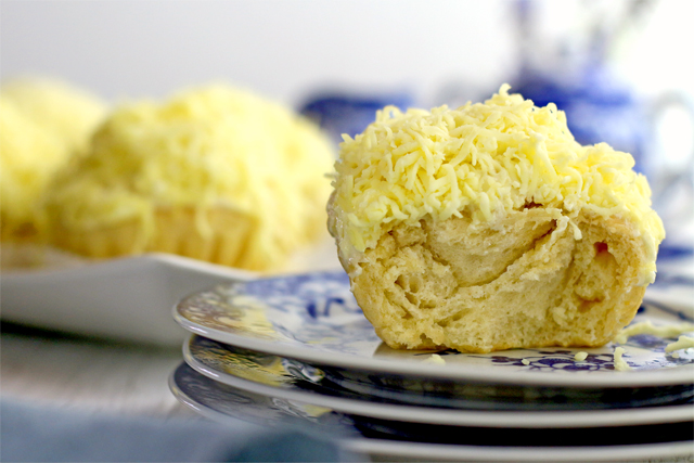 One yellow Ensaymada is on a stack of blue and white plates with another plate full of Ensaymadas in the background