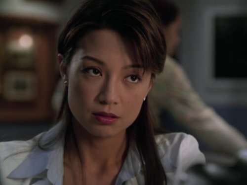 Ming-Na Wen as Dr. Jing-Mei "Deb" Chen. Her head is tilted and she is looking off in the distance at someone behind the camera. Behind her is a blurry image of a person.