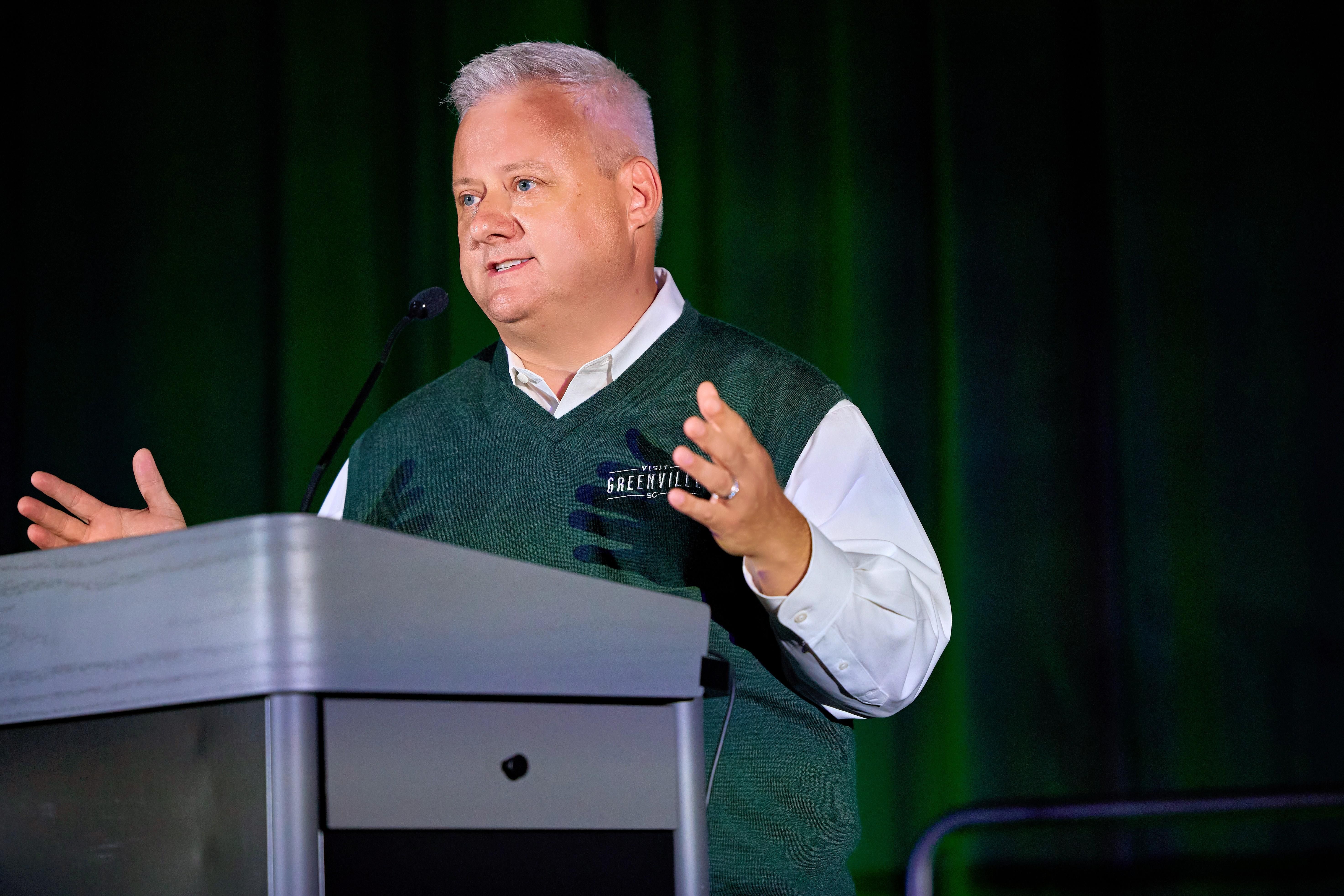 A man speaking on stage representing Visit Greenville.