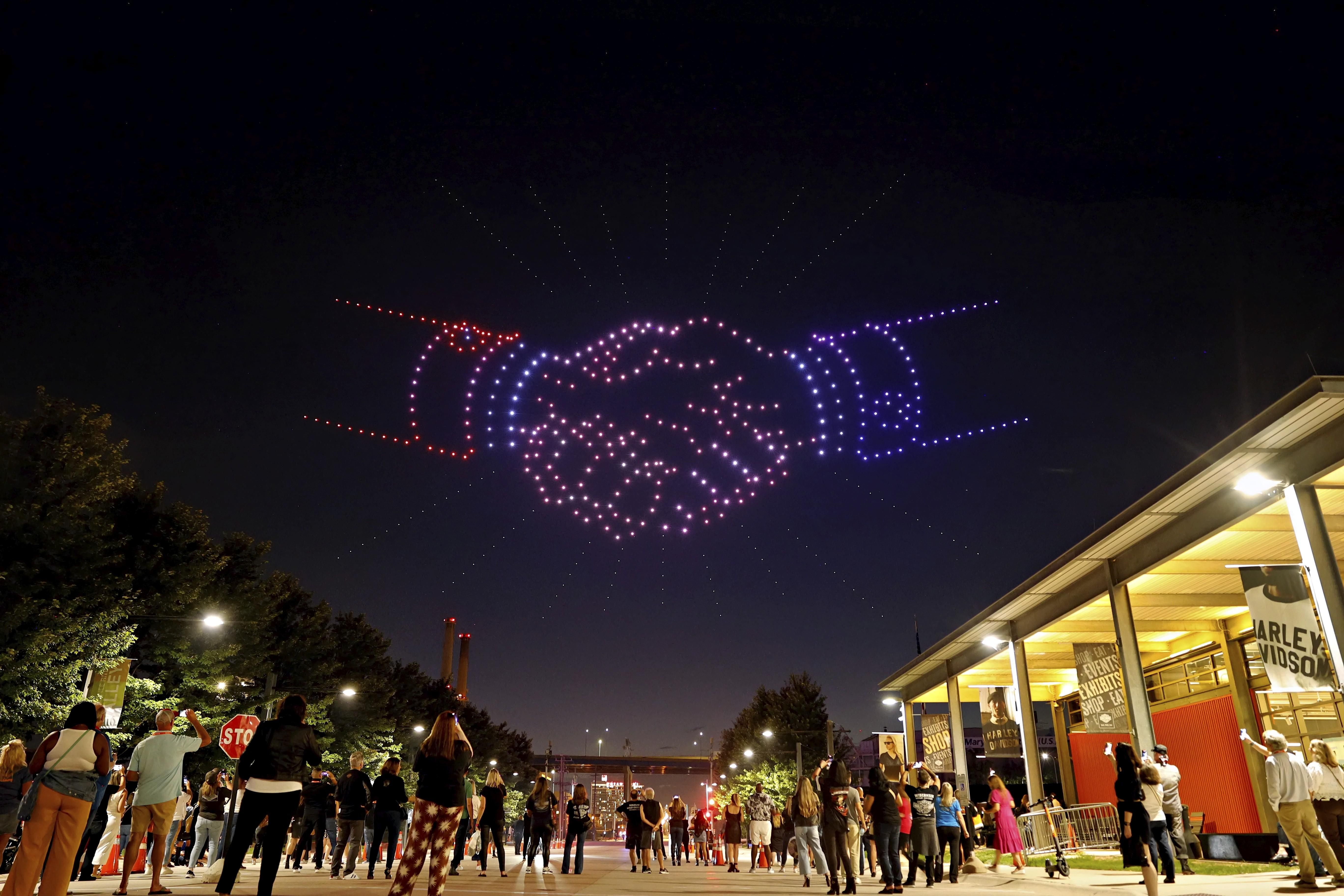 A drone show with two hands sharing in the sky.