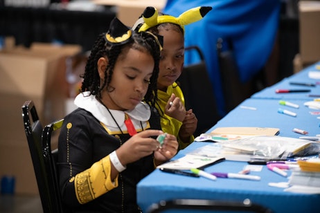 Two children, one dressed as Shpinx, the other at Pikachu, creating art and coloring in the Kids' Lab