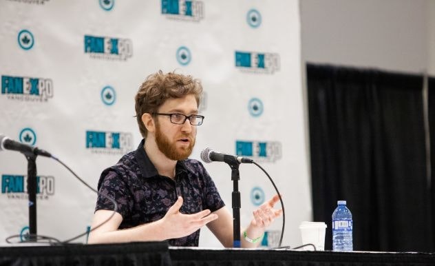 Voice actor Justin Briner raises both hands as he answers a question on stage