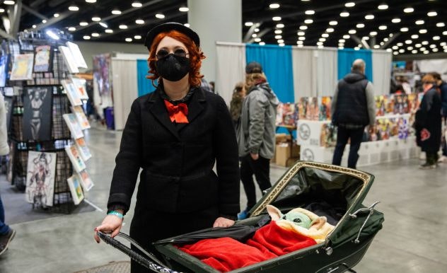 A cosplayer wearing all black pushes a baby Grogu in a carriage