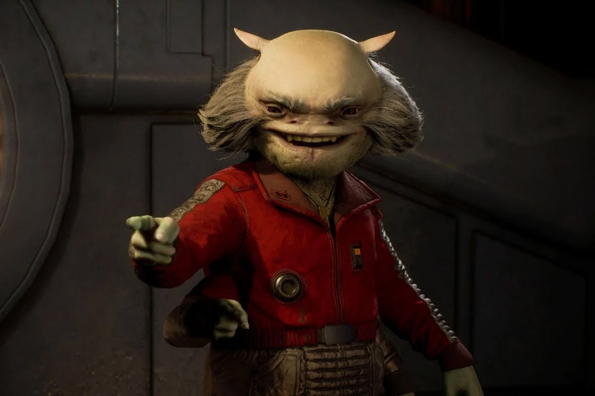 Greez, wearing a red leather jacket, points one of his four arms at someone while smiling