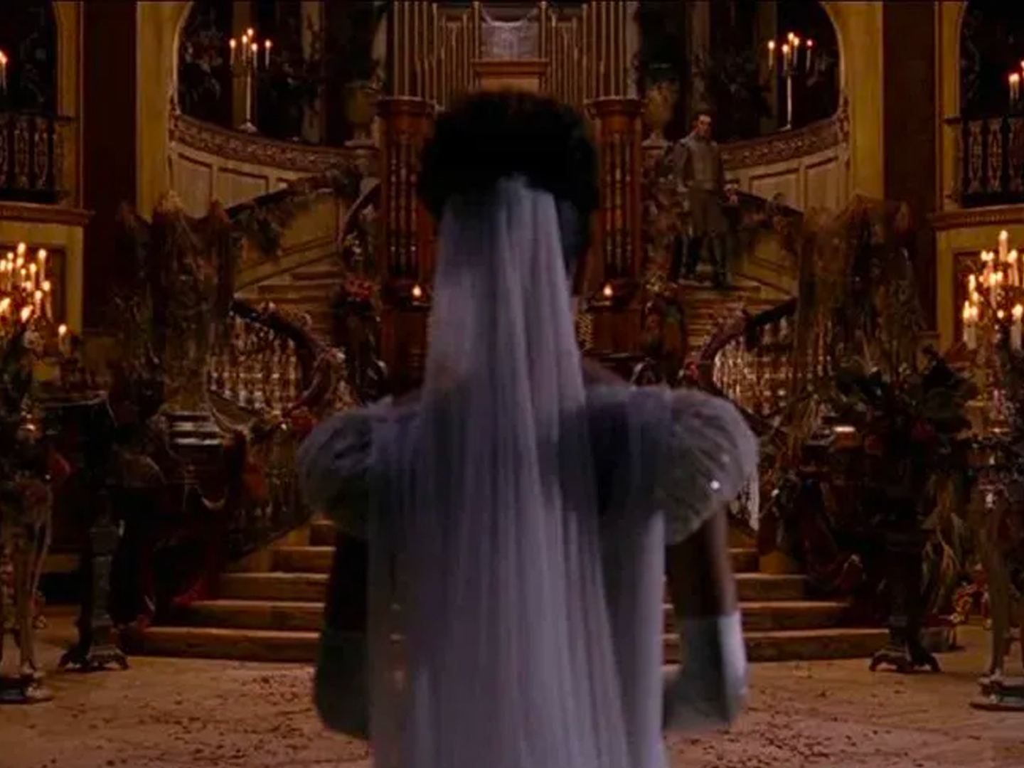 A person wearing curtains as if they were a ghost stands in a foyer