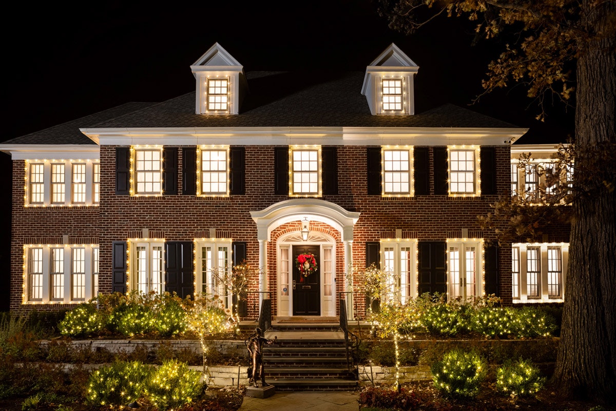 The grand home with a long tile pathway at dusk. The porch light is on giving a golden glow to the doorway