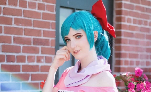 Corpsekid Cosplay poses in a pink shirt and blue wig with a red bow