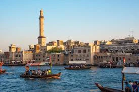 Traditional wooden boats, known as abras, ferrying passengers on a waterway with historic buildings and a tall minaret in the background.