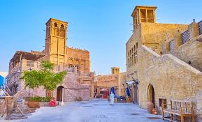 A historical district featuring traditional Middle Eastern architecture with wind towers, narrow alleys, and stone buildings under a clear blue sky.