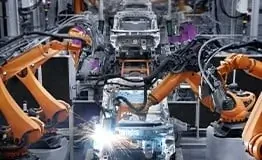 Linha de montagem automotiva robótica com múltiplos braços KUKA articulados laranja realizando operações de soldagem e montagem de carrocerias de veículos com faíscas visíveis, exemplificando a automação na Indústria 4.0.