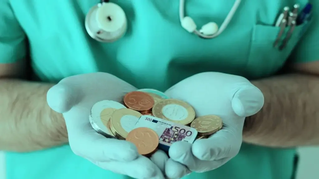 Profissional de saúde com luvas cirúrgicas segurando moedas e uma réplica de nota de Euro nas mãos. Conceito de custos hospitalares, financiamento da saúde e economia médica.