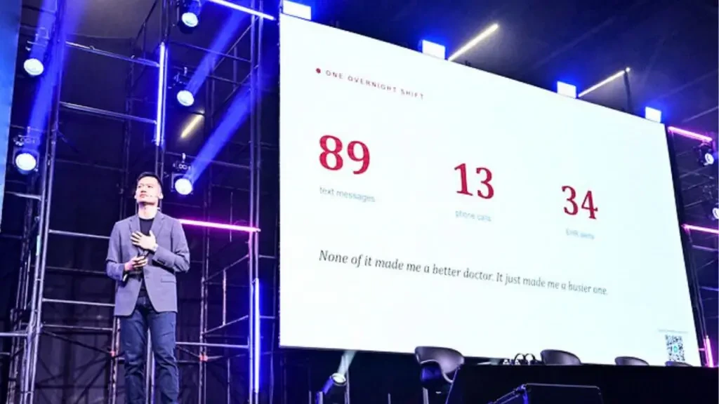 Brian Han palestrando no evento HIS sobre o uso de Inteligência Artificial na saúde diante de uma grande tela de apresentação.