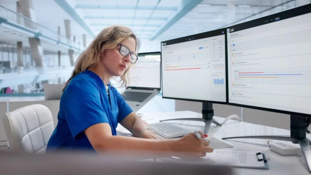 Profissional de saúde analisa dados em monitores com sistema EHR, ilustrando a interoperabilidade na saúde digital.