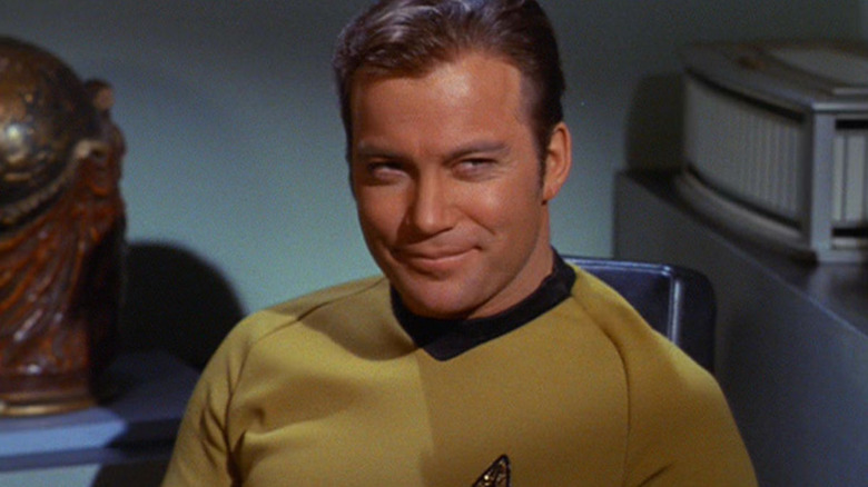 Captain Kirk sits in his office, wearing his signature yellow tunic. He smirks at another character off screen