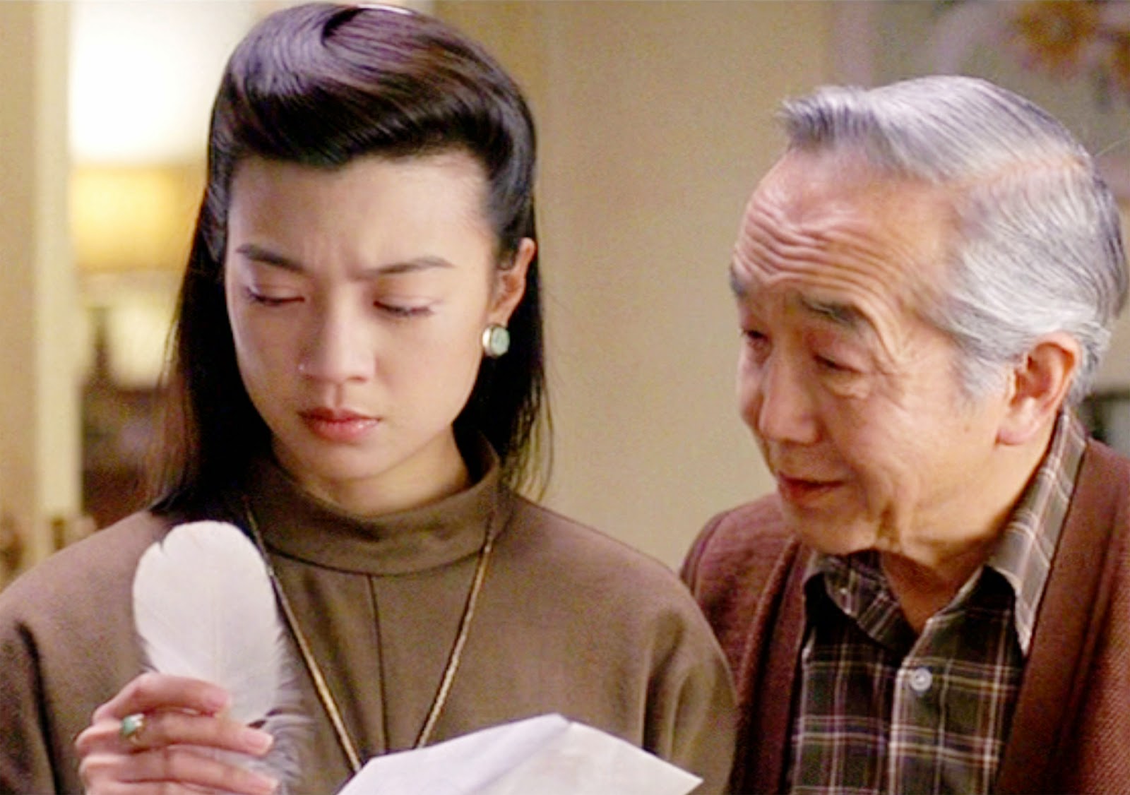 Ming-Na Wen holding a white feather and looking at it with an older gentleman