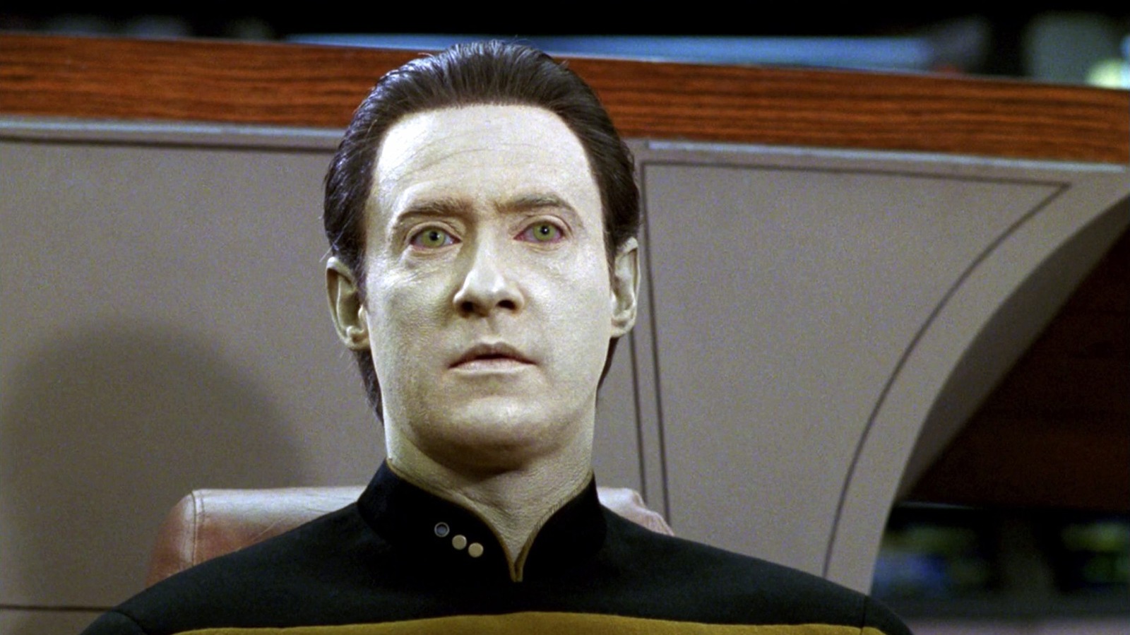 Data stands in front of a wall on the Starship Enterprise- his ghost white skin, and matching white eyes look forward in a look of confusion.