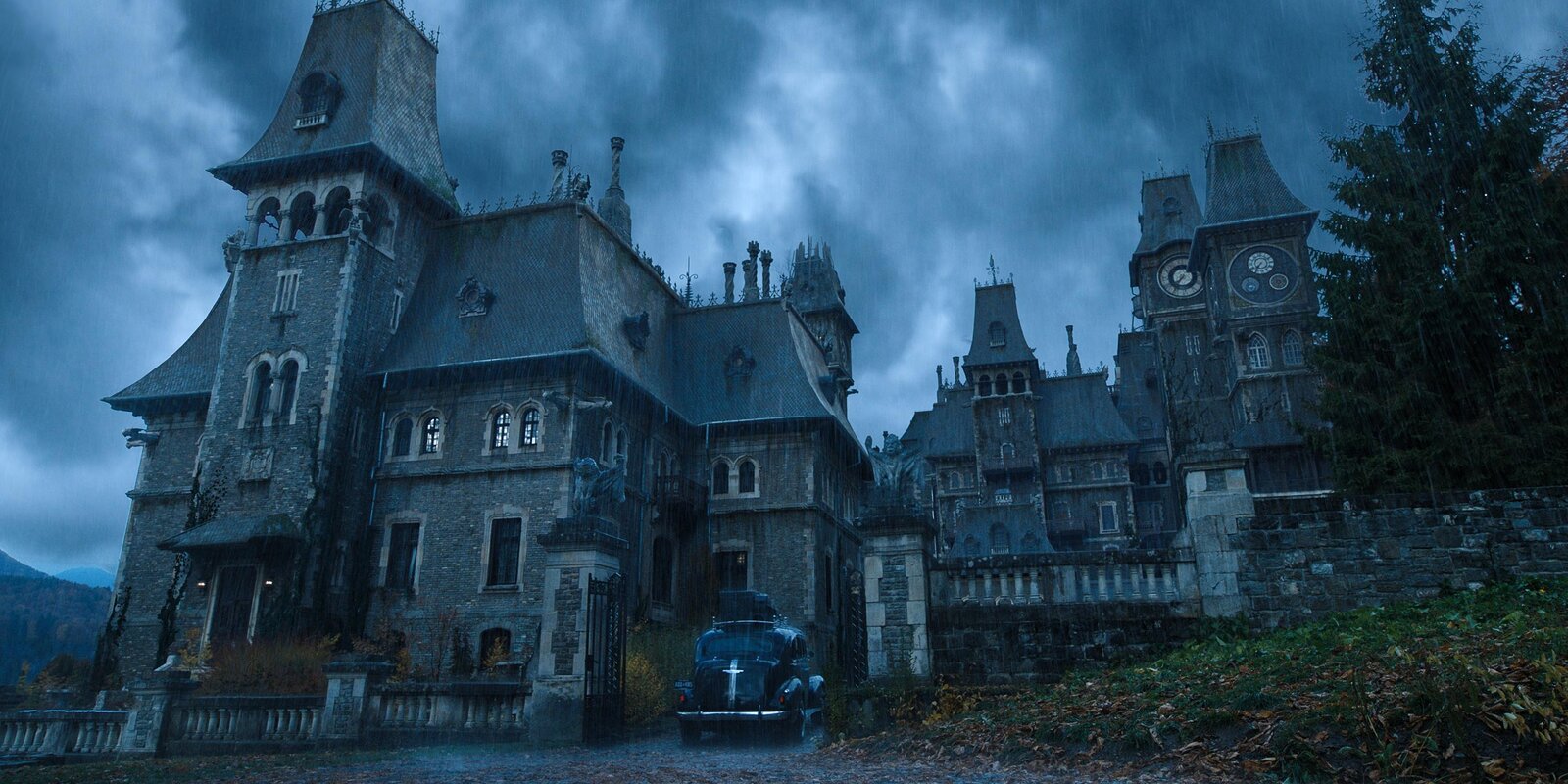 The mansion stands on a hill top, with the car in the stone driveway. The backdrop is cloudy and grey, and the house, a pale blue grey in comparison