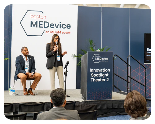 Two people at a podium with a microphone, engaging in a dialogue on "Learning Built Around Real Challenges.