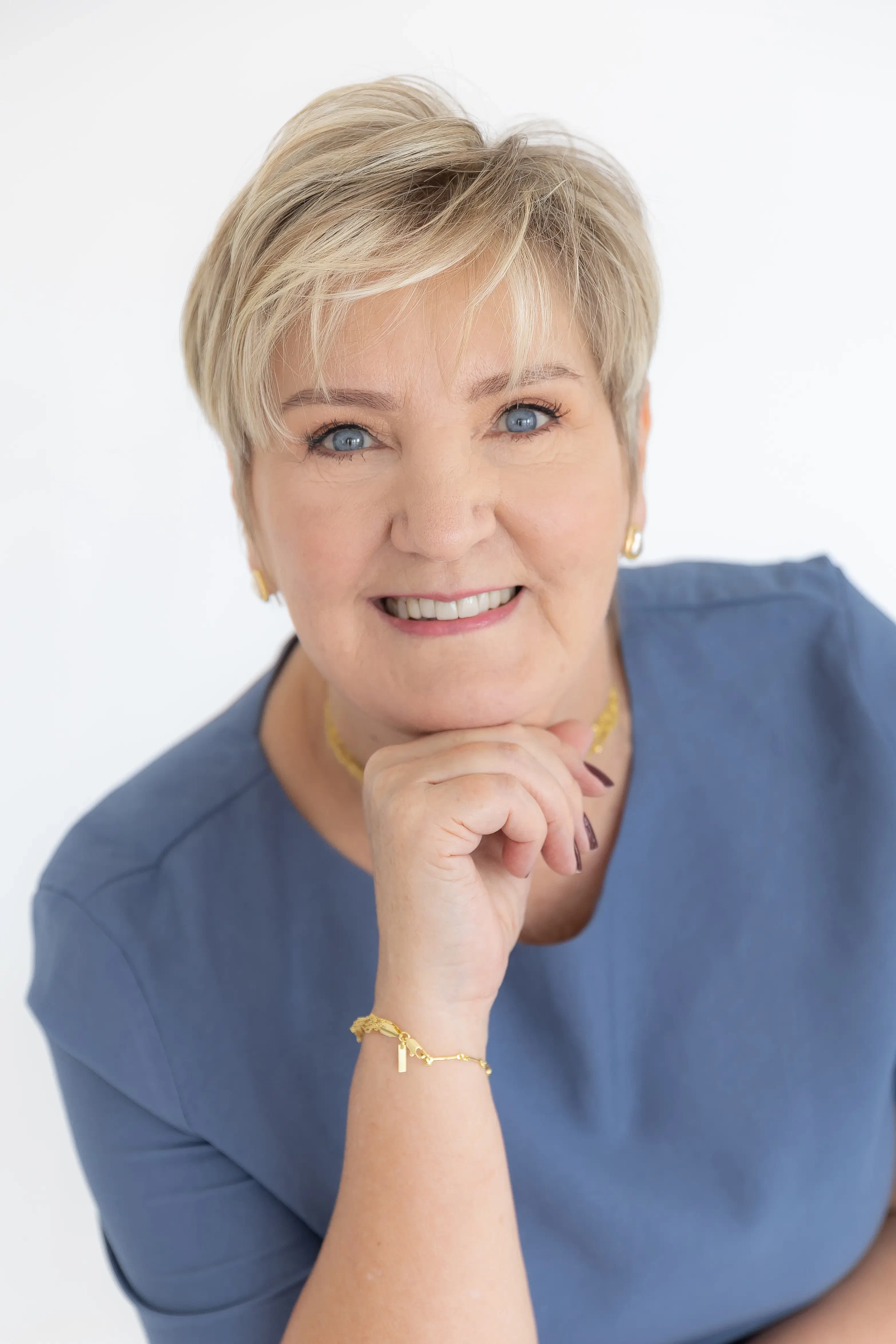 Leonisa Scholz Obrusnik, especialista em saúde e curadora do CSC - Congresso de Supply Chain 2026, posa sorrindo com o queixo apoiado na mão. Foto profissional em estúdio com fundo branco, vestindo blusa azul.