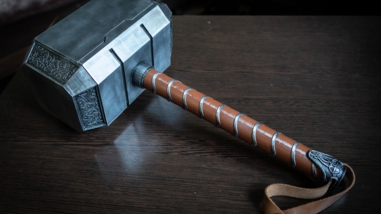 Mjolnir laying on a dark wood table top, handle turned toward the screen