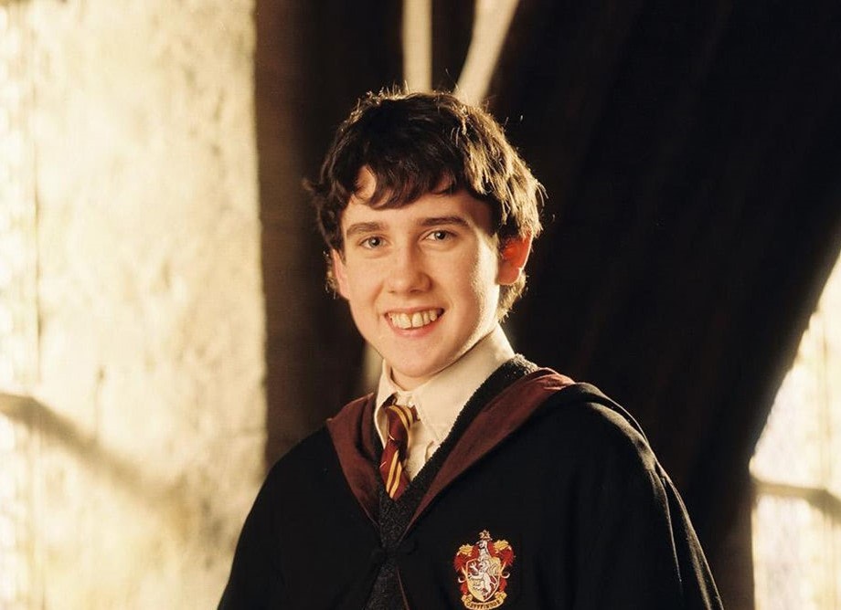 Nevill in his Gryffindor robes, smiling and posing for a picture