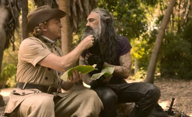 Man in old-fashioned khakis intimately picks food out of fellow pirate's beard