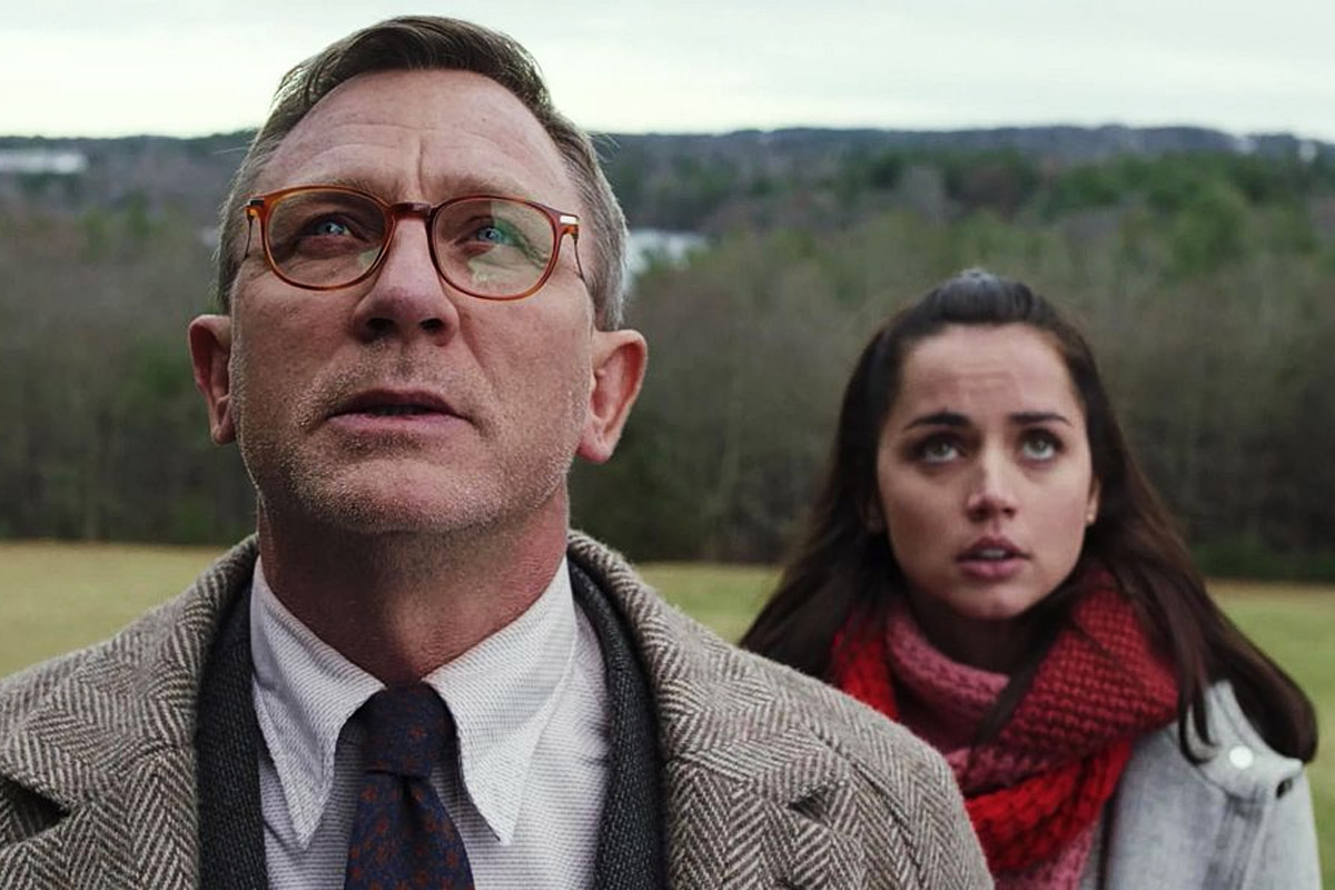Daniel Craig & Ana De Armas look up with a beautiful mountain landscape behind them