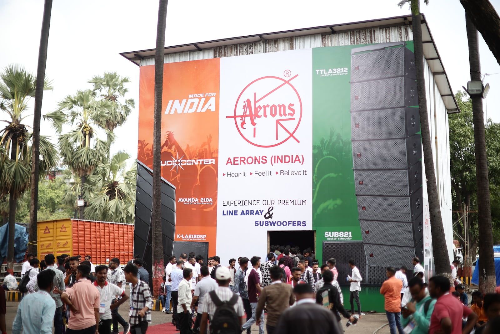 Crowd gathered outside the Demo Qube booth at PALM Expo, featuring large promotional banners for premium line array speakers and subwoofers.