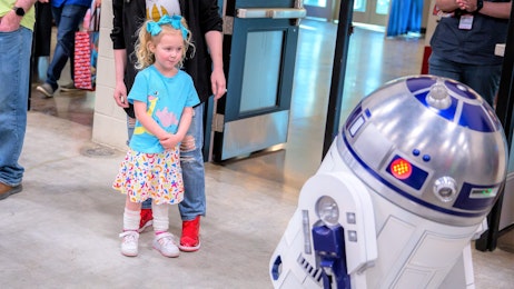 A young girl looks at R2D2 on the show floor