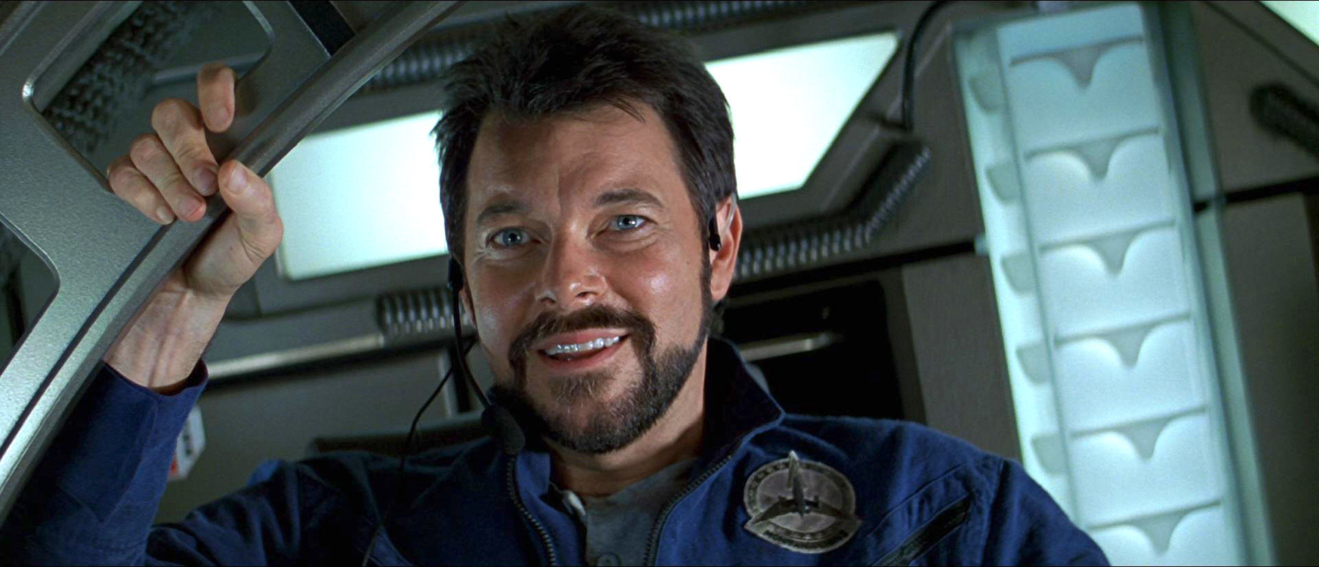 William Riker holds on to the door of the enterprise - donning his blue work suit, he smiles at a team success