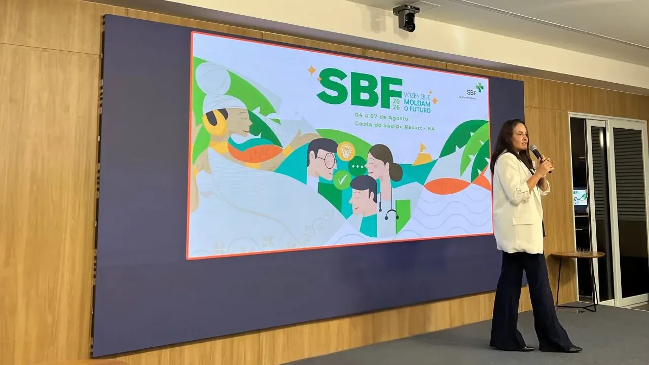Palestrante no palco do Saúde Business Fórum (SBF) 2026. Ao fundo, tela com a identidade visual do evento "SBF 2026: Vozes que moldam o futuro", que acontecerá de 04 a 07 de agosto no Costa do Sauípe Resort, Bahia.