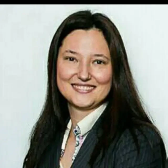 Retrato de Sonia Poloni, CEO da ABCIS. Uma mulher de cabelos longos e escuros, sorrindo, vestindo um blazer escuro com estampa sutil de risca de giz sobre uma camisa social clara.