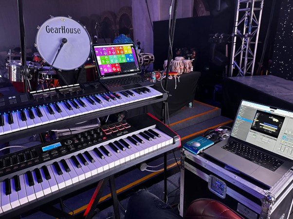 A stage setup featuring professional audio gear with multiple keyboards, a laptop running sound software, and monitoring equipment prepared for a live performance.