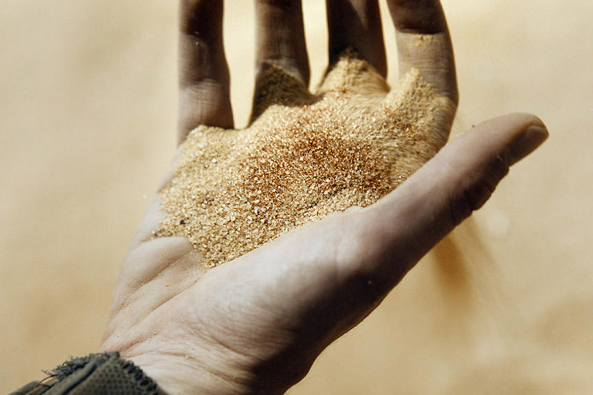 A hand holds spices that are overflowing above a sandy floor